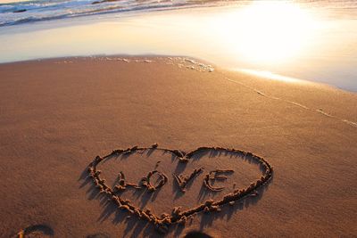 High angle view of heart shape with text on wet shore during sunset