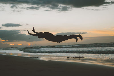 Silhouette man jumping over beach against sky during sunset