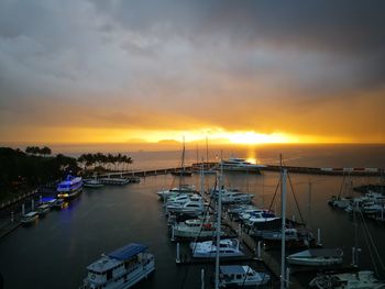 Sailboats moored at harbor against sky during sunset