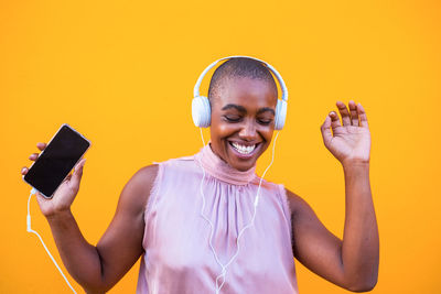 Smiling woman listening music against yellow background