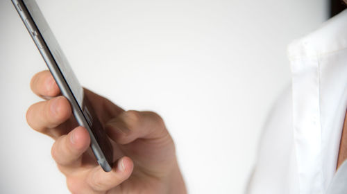 Cropped image of hand using mobile phone against white background