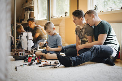 Homosexual fathers looking at son playing while making toy boat at home