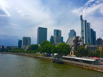 River by modern buildings against sky in city