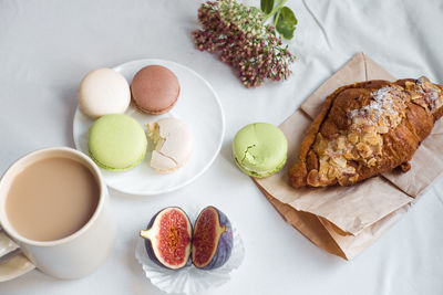 Aesthetics of a cup of coffee, figs, a large croissant and macarons on a white background, top view