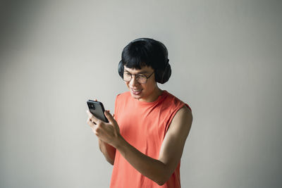 Young man using mobile phone against wall