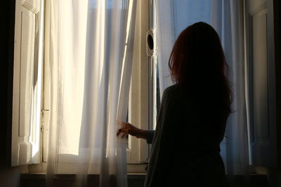 Side view of woman looking through window at home