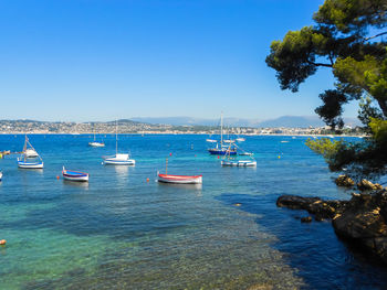 Boats in sea against clear blue sky