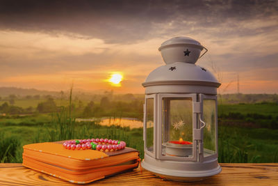 Lit candle and purse with necklace on table against sky during sunset