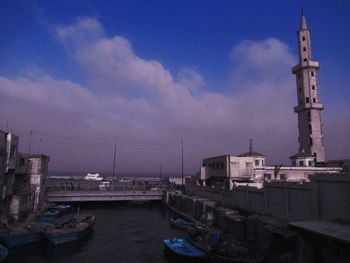 Boats moored at harbor by buildings in city against sky
