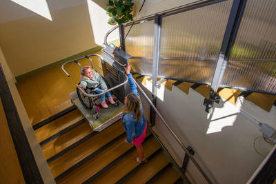 Mother and child living with cerebral palsy using wheelchair lift to access public building.