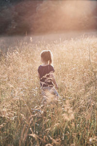 Rear view of girl standing amidst plants on field