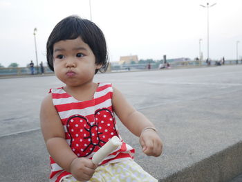 Cute girl sitting on street against clear sky