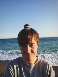 Portrait of young man with pebbles on head at beach against clear sky