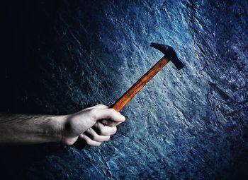 Cropped hand of man holding hammer against wall