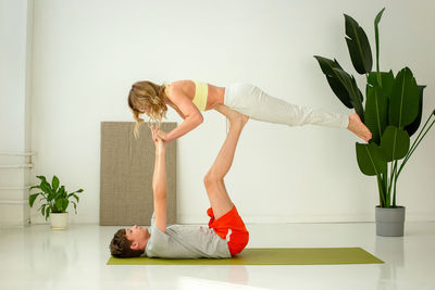 A guy  lies on a sports mat, does yoga in a pair with a woman, doing exercises with support.