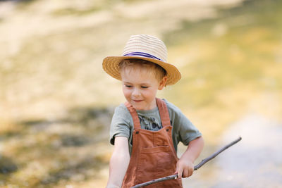 Preschooler boy plays fishing, child fishes with stick near lake in countryside, games in nature