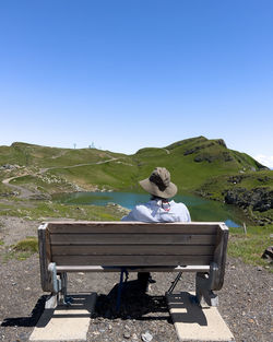 Rear view of man sitting on bench against clear blue sky
