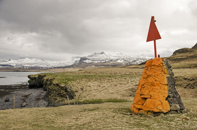 Orange painted rocks with a red steel sign, as a navigation symbol on the coast in iceland