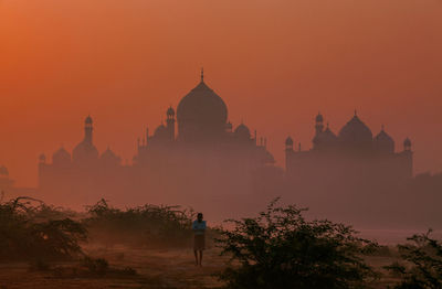 Man standing on field with silhouette taj mahal in background during sunrise