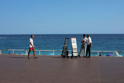 Rear view of couple standing on beach against clear sky