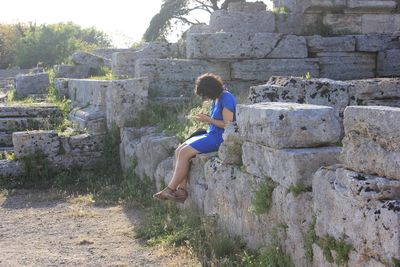 Side view of woman using smart phone sitting on stone wall