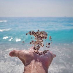 Cropped hand throwing pebbles against sea