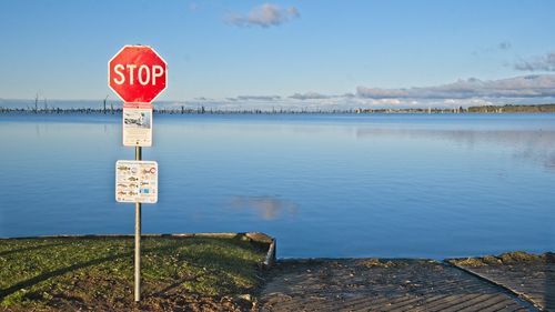 Road sign by lake against sky