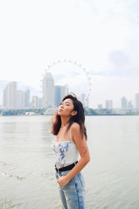 Beautiful young woman standing against sea in city