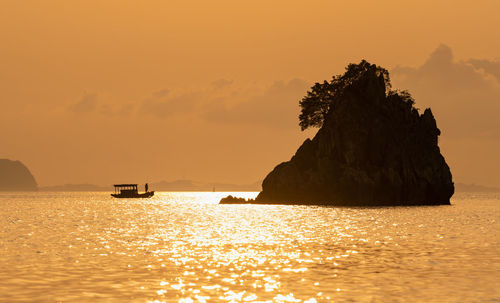 Silhouette rocks in sea against sky during sunset