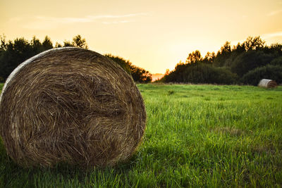 Hay bales on field against sky during sunset