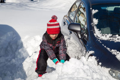 High angle view of boy playing with snow by car