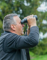 Side view of mature man looking through binoculars in forest