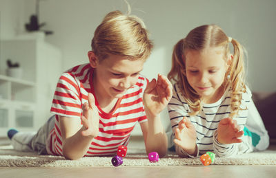 Cute sibling playing with dice on floor at home
