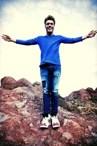 Portrait of young man standing on rock formation against sky
