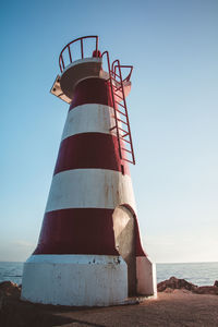 Lighthouse by sea against clear sky