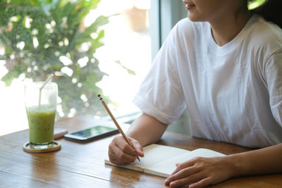 Midsection of woman holding glass while sitting on table