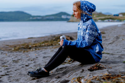 Young woman holding insulated drink container while sitting at beach