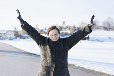 Portrait of smiling senior woman with arms outstretched on road during winter