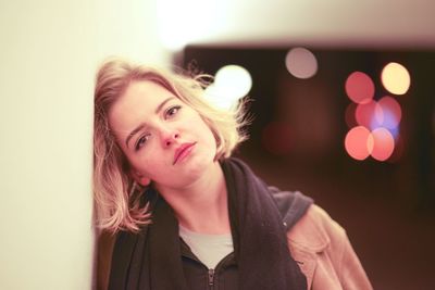 Portrait of beautiful young woman against illuminated wall