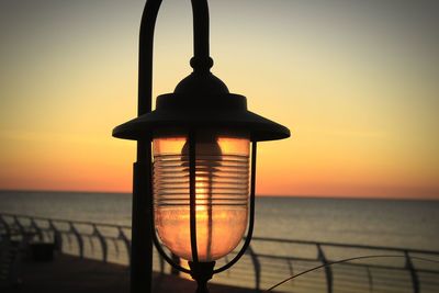 Silhouette lantern on beach against sky during sunset