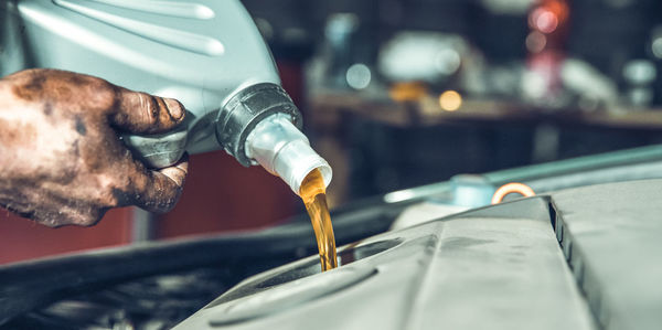 Cropped hand of mechanic pouring motor oil in vehicle
