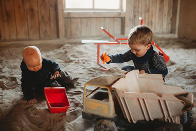 Brothers playing with trucks and shovels in outdoor sandbox in winter