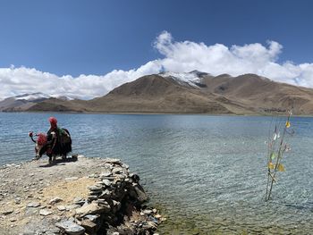 Man sitting by lake against sky