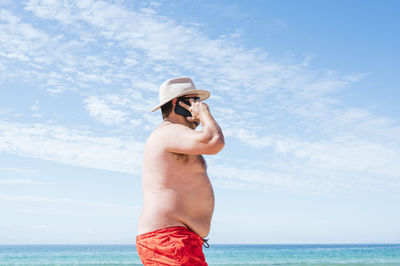 Mature overweight man talking on smart phone at beach during vacation