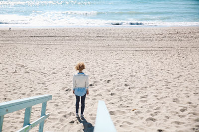 Rear view of mid adult woman standing at beach