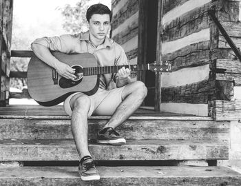 Portrait of young man with acoustic guitar sitting porch steps