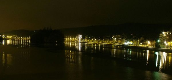 Illuminated city by river against sky at night