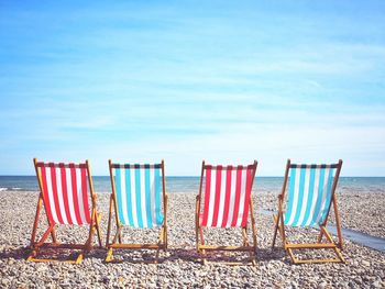 Empty deck chairs at beach against sky