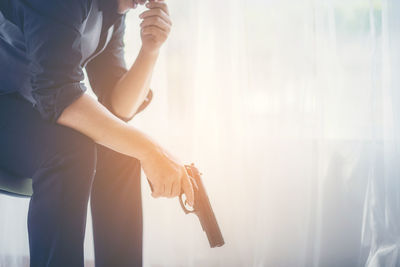 Midsection of woman holding curtain at home