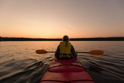 Woman kayaking in lake against sky during sunset